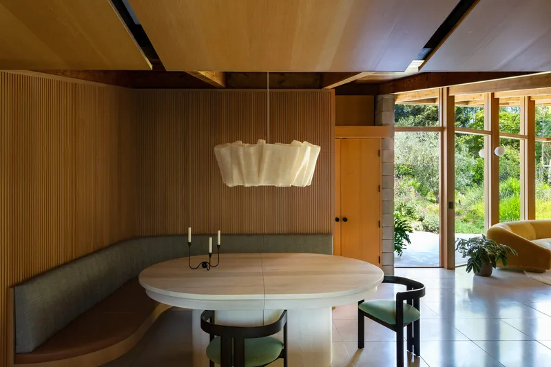 Dining area with curved built-in bench, ribbed wood walls and plywood ceiling with exposed black steel beams