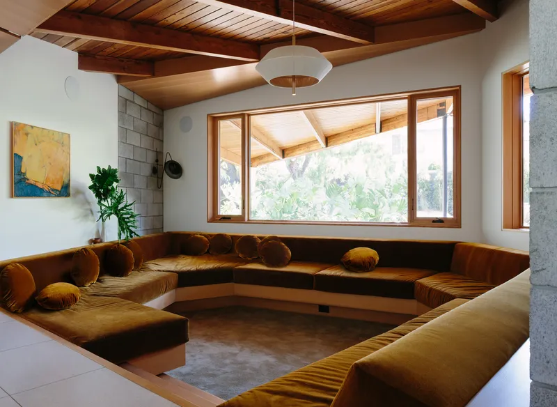 Sunken conversation pit with burnt orange upholstered seating beneath exposed timber rafters and clerestory windows
