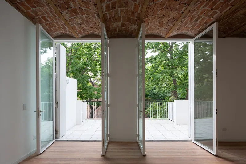 Room with exposed brick barrel vault ceiling opening to twin balconies framed by glass doors