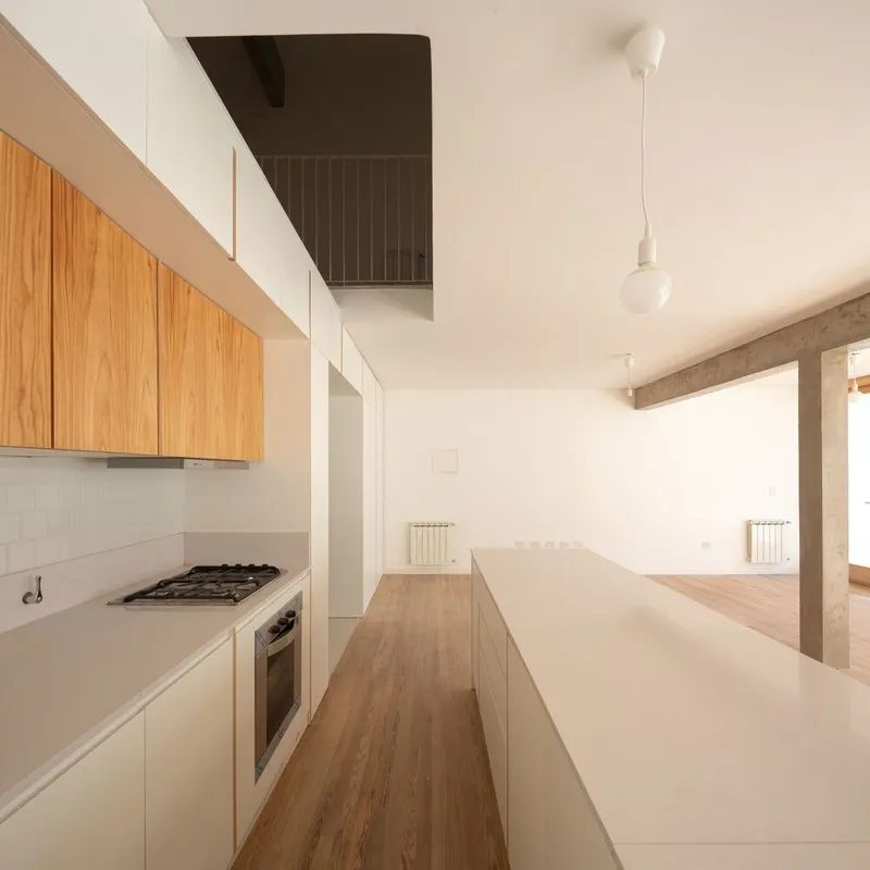 Galley kitchen with timber and white cabinetry leading to open living space with concrete beam