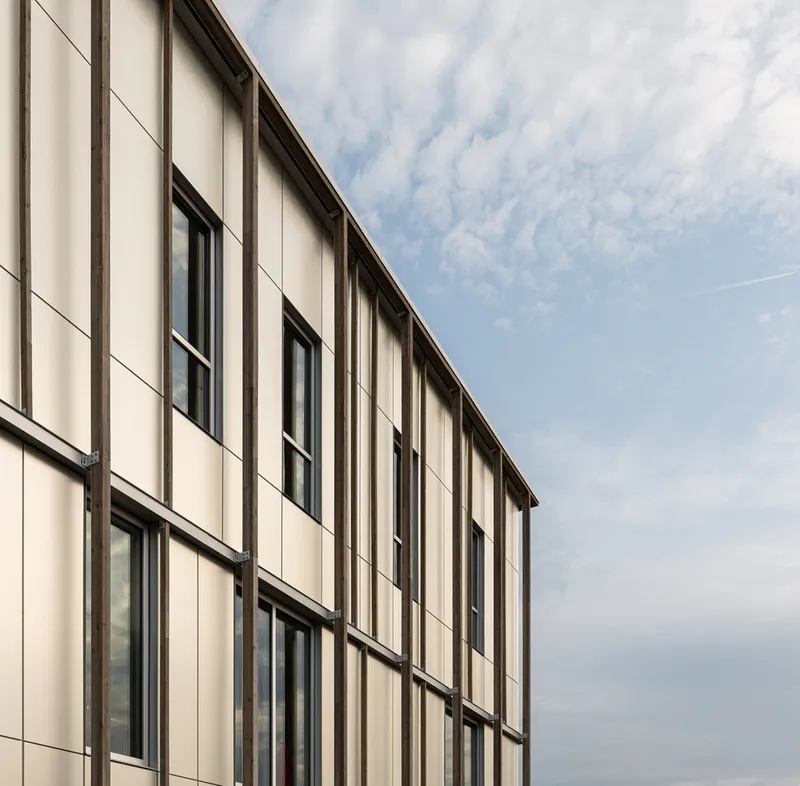 Angled view of the striped timber facade and punched windows against a partly cloudy sky