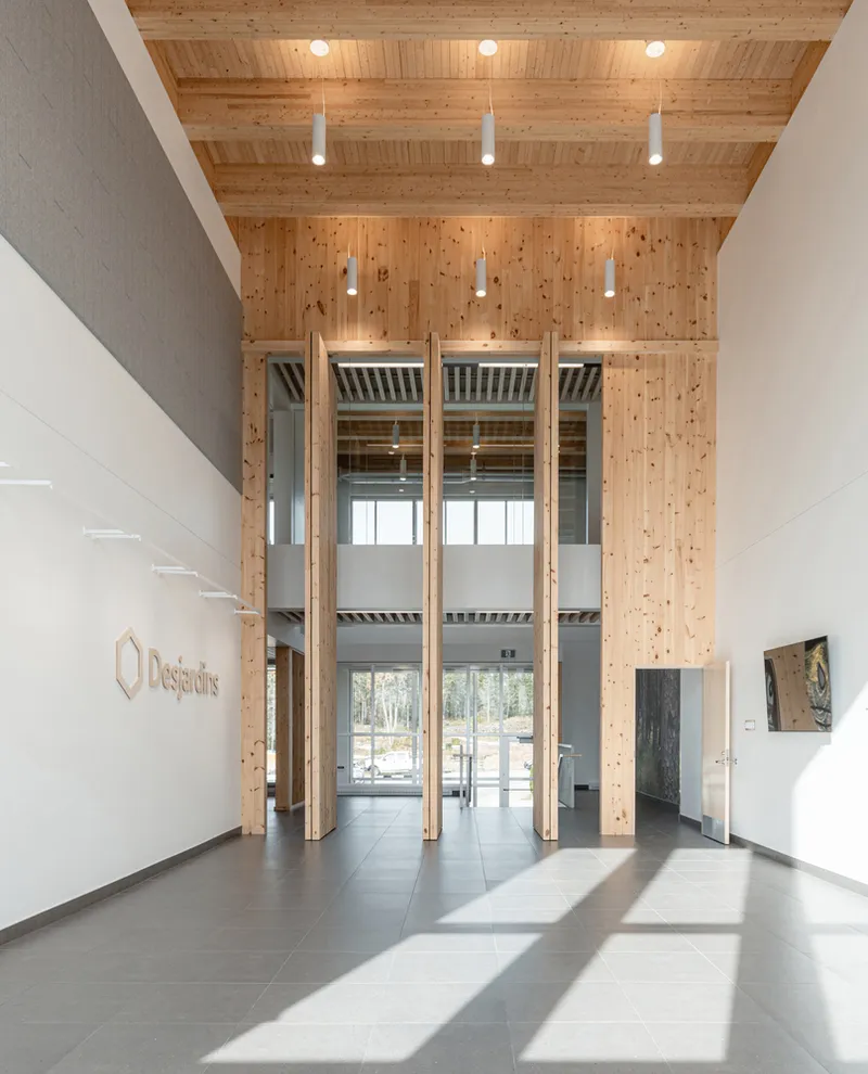 Tall glazed entrance doors framed in timber opening to reveal a double-height lobby beyond