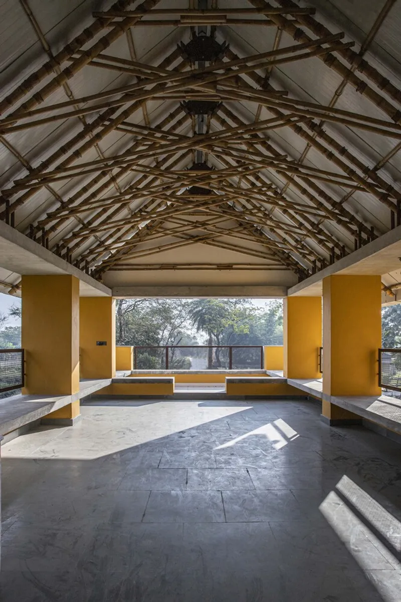 Open-air hall with exposed timber truss roof and yellow columns overlooking a courtyard in morning light