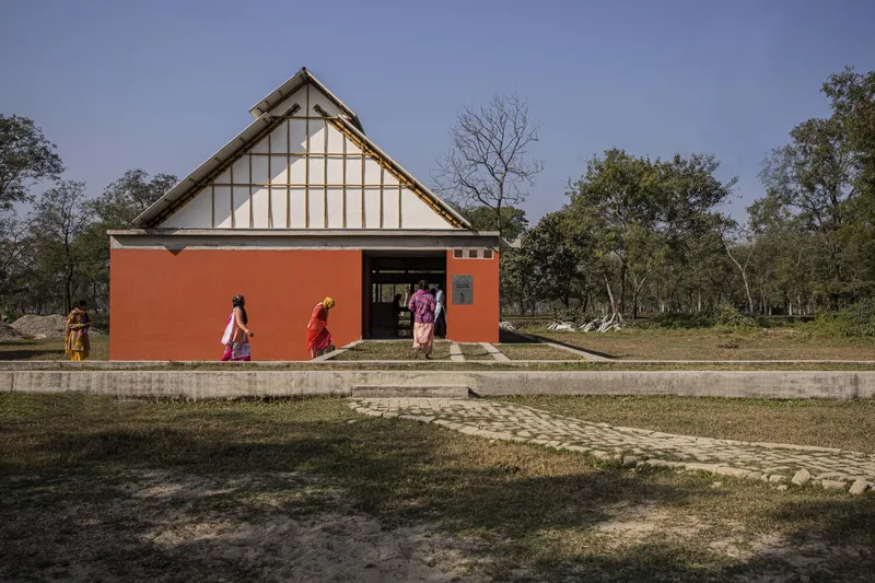 Red facade with timber gable roof and people in colorful garments walking along a concrete pathway