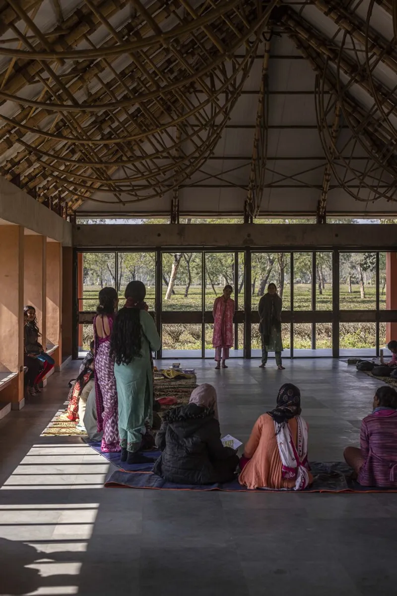Gathered visitors seated on the floor beneath the vaulted timber roof facing the glazed wall and landscape