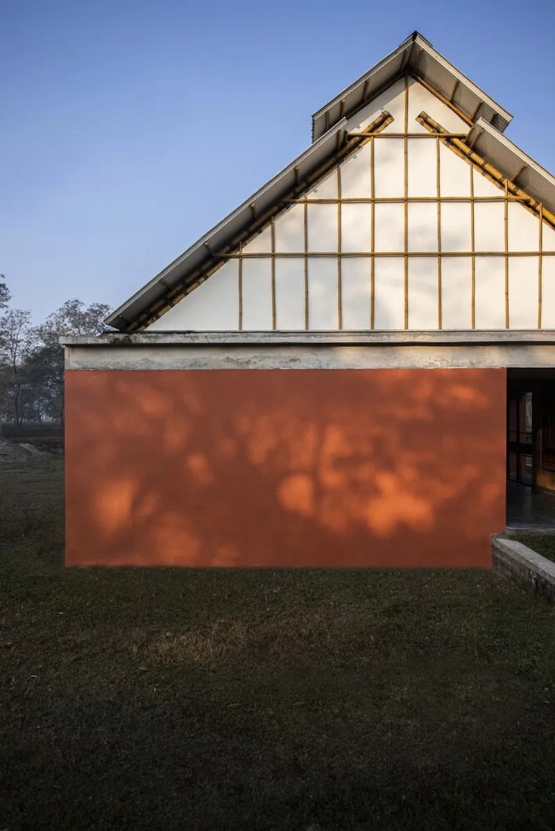 Exterior view of timber-framed gable wall with translucent panels above a rust-colored volume at dusk