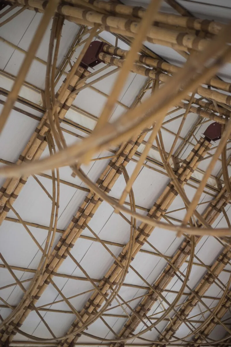 Close-up of the curved bamboo lattice structure with bundled joints and metal connectors overhead