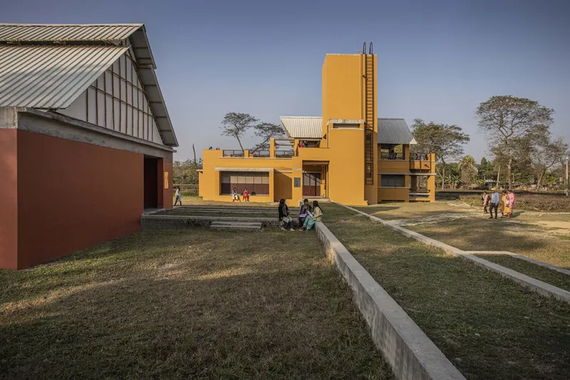 Yellow stucco building with a central tower and stepped grass terraces with people sitting in afternoon light