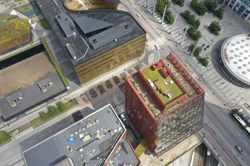 Aerial view of the green roof courtyard surrounded by red perforated metal facades and neighboring towers