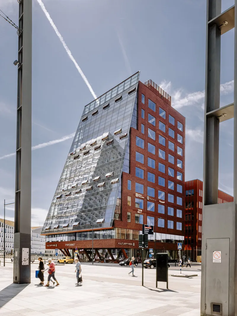 Pedestrians crossing the plaza in front of the faceted glass and brick volume with retail base