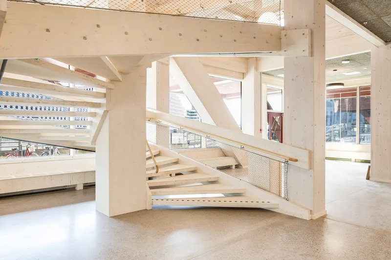 Light timber staircase with mesh panel balustrade ascending between exposed cross-laminated timber beams and columns