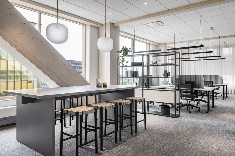 Open office workspace with dark communal table, timber stools, exposed diagonal timber beam and suspended globe pendants