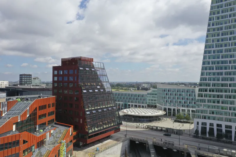 Aerial view of the sloping dark brick facade with operable windows beside an orange paneled structure