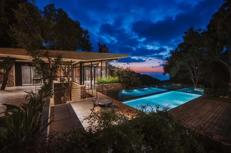 Illuminated terrace and infinity pool with timber deck at dusk under deep blue clouds