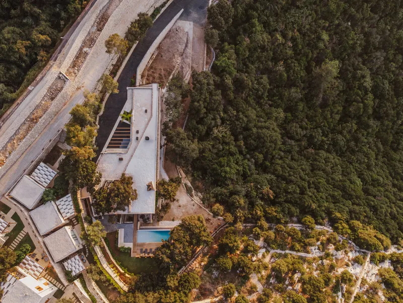 Drone view showing the concrete rooftop terrace and pool nestled into the sloping wooded terrain