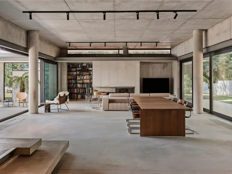 Living area with concrete ceiling, cylindrical columns and floor-to-ceiling windows overlooking the lawn