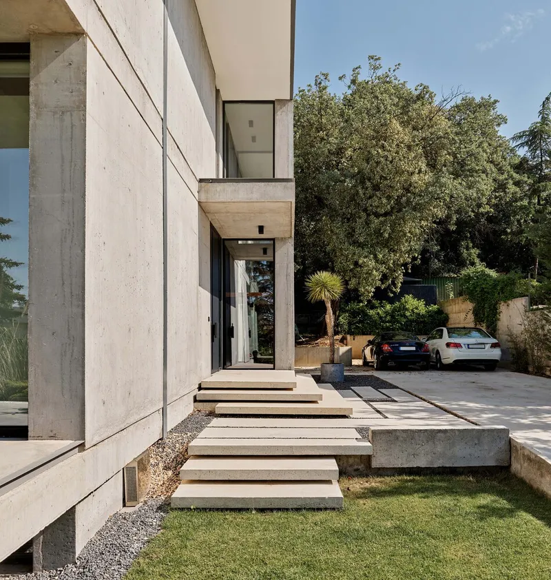 Cantilevered concrete entrance steps leading from lawn to driveway with mature trees beyond