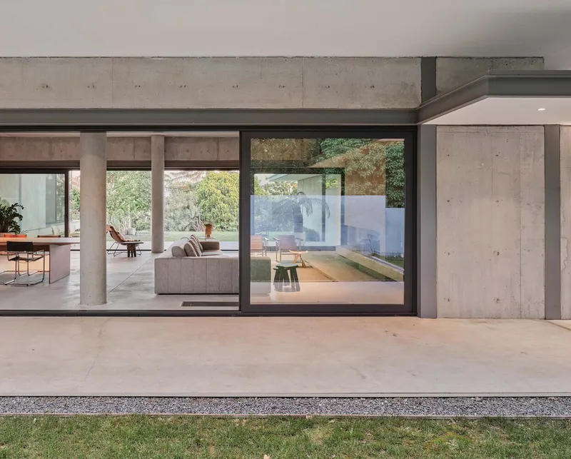 Black-framed glass wall separating interior living spaces from a covered concrete terrace at dusk