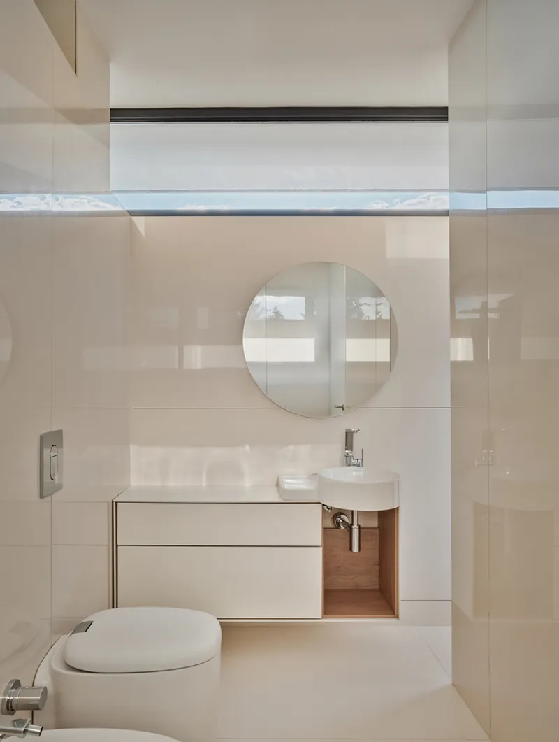 Bathroom with pale tile walls, round mirror, and clerestory window above the vanity