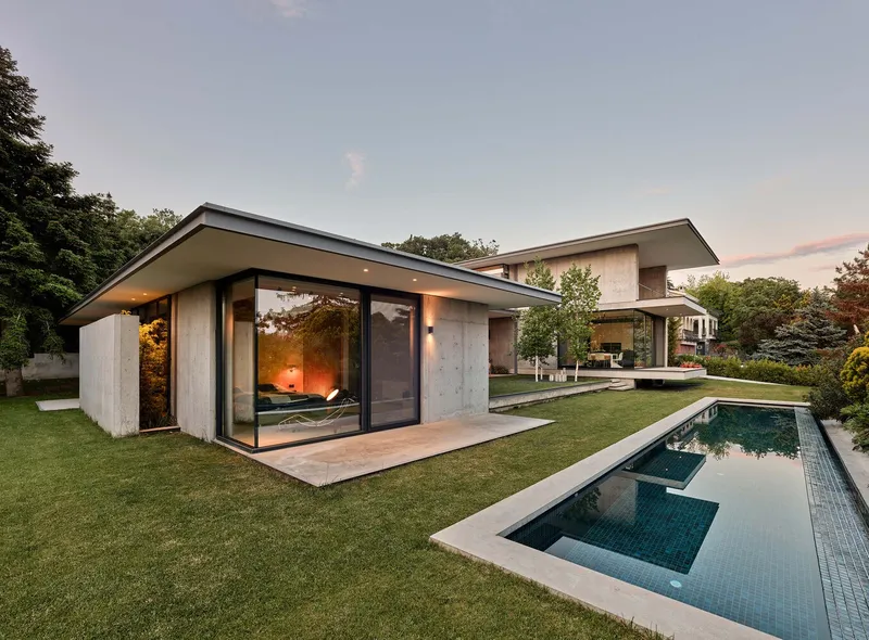 Garden view of the concrete pool house pavilion with full-height glass doors at dusk