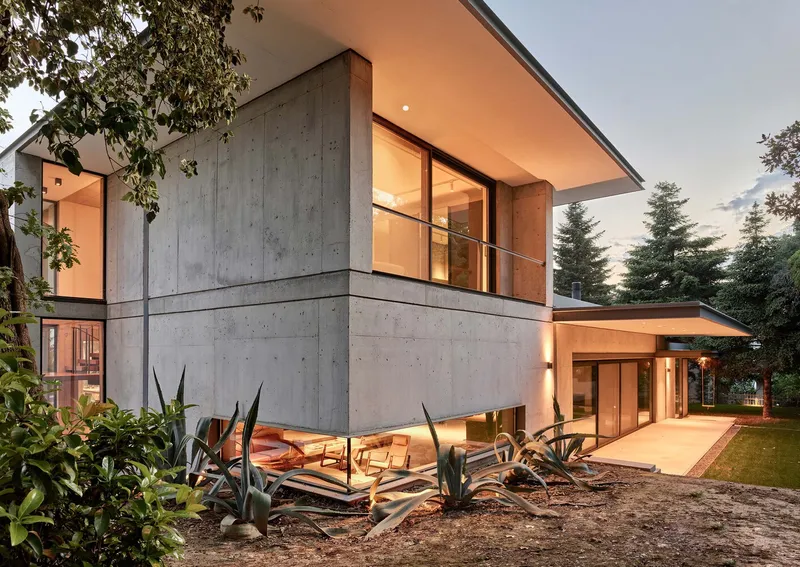 Two-storey concrete facade corner with planted agave garden and cantilevered roof overhang at twilight