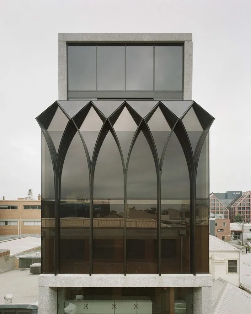 Facade with dark arched metal frames and glass panels topped by a concrete volume with sliding windows