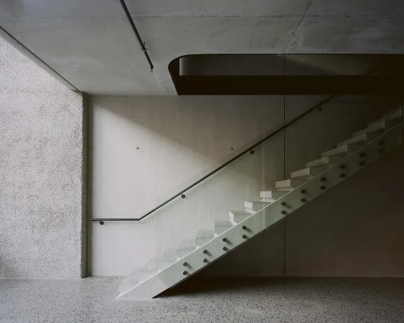 Concrete staircase with steel handrail and glass balustrade casting diagonal shadows on the wall