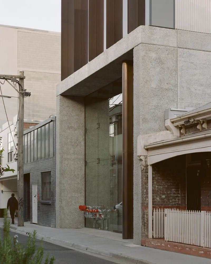 Street view showing concrete columns supporting a cantilevered volume clad in bronze metal panels