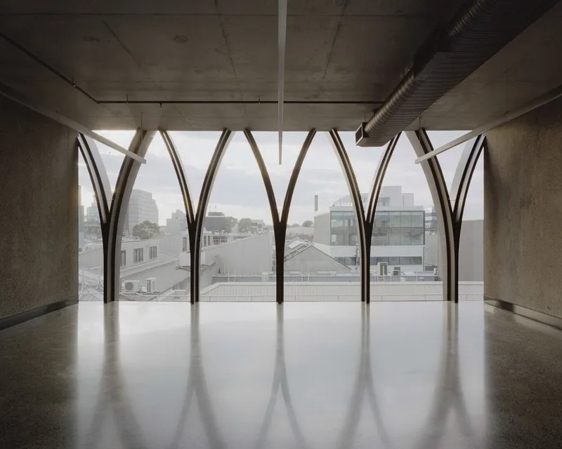 Interior space with polished concrete floor beneath arched metal frames framing rooftop views through mist