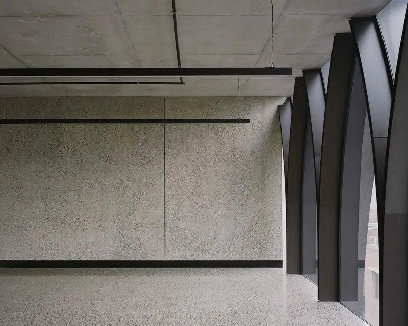Terrazzo floor meeting exposed concrete wall panels beside dark metal arched screen elements