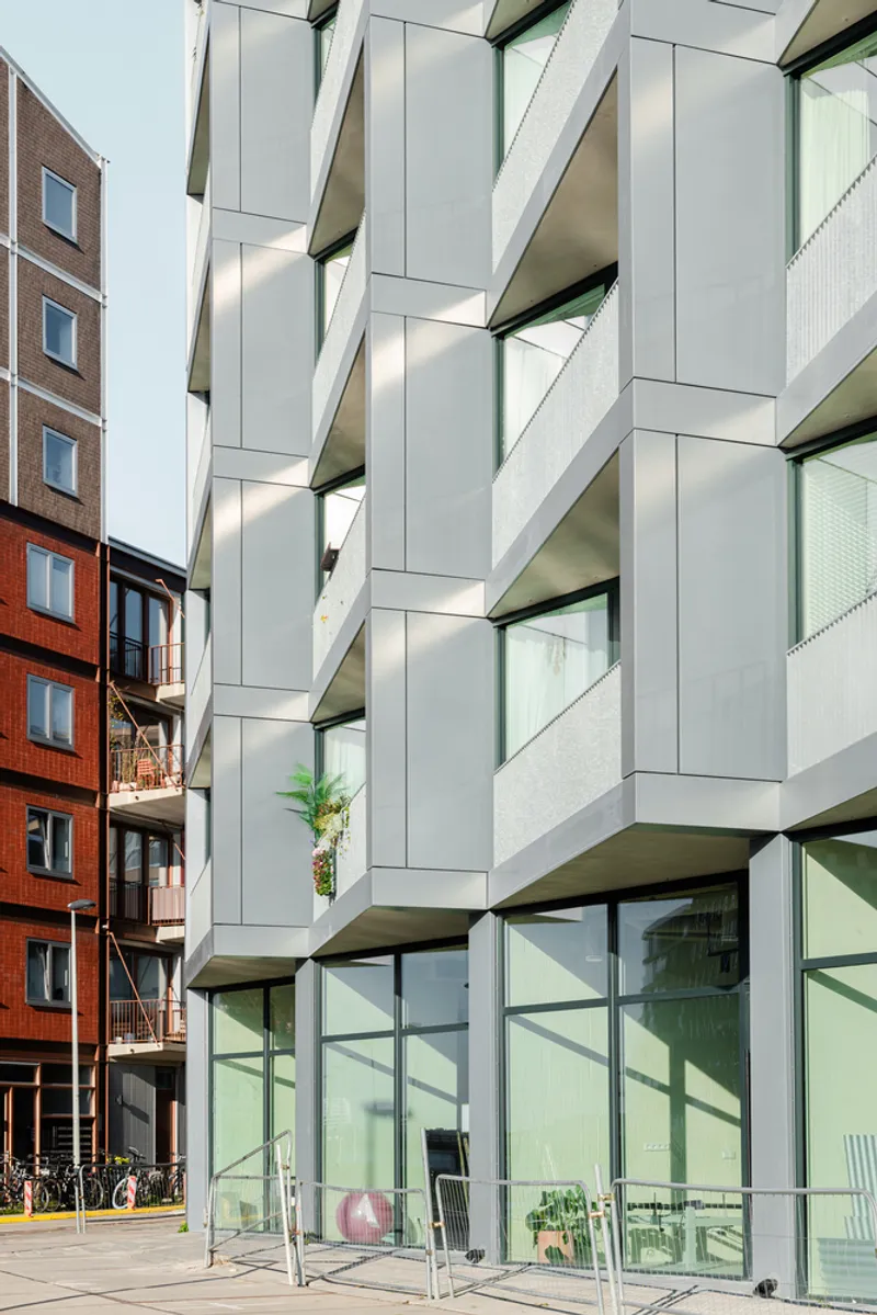 Angled concrete balconies with metal panel cladding adjacent to an existing brick apartment building