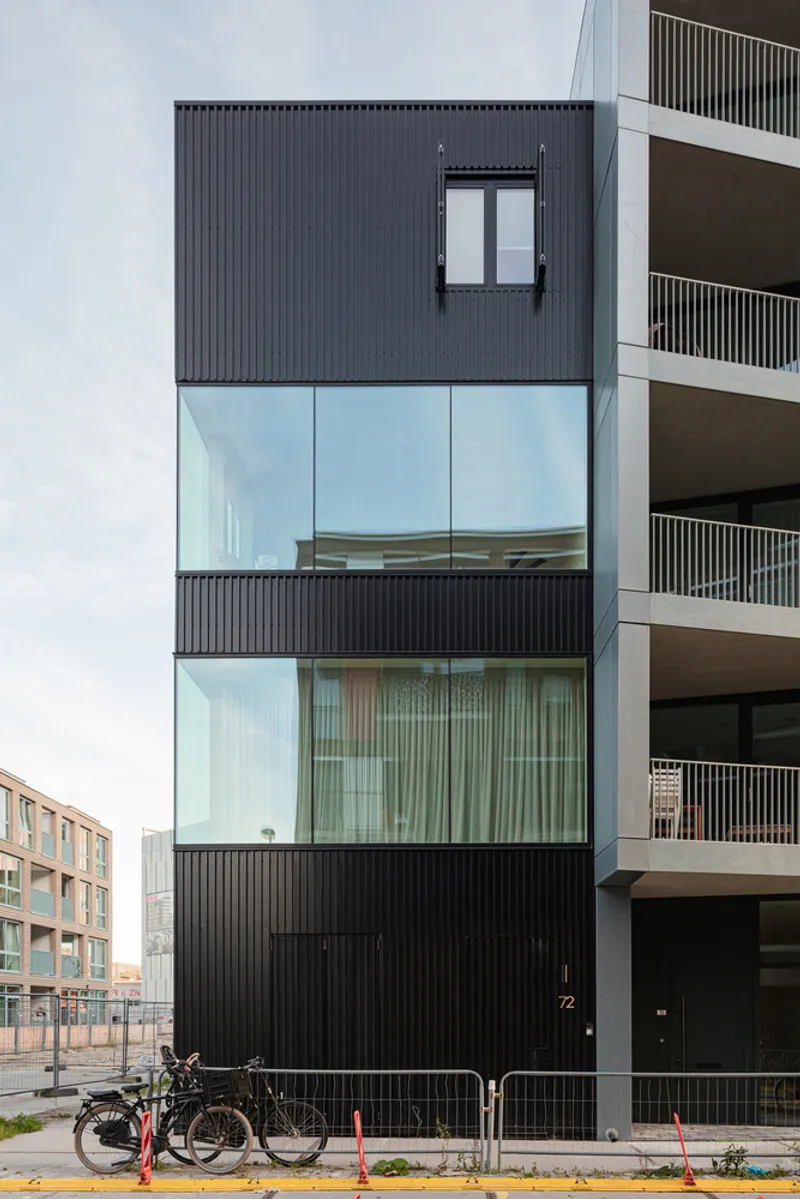 Black corrugated metal townhouse facade with full-height glass balcony and parked bicycles at street level