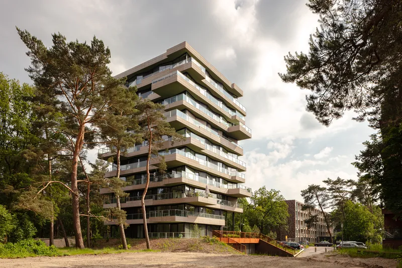 Stacked balcony tower rising above pine trees with an orange pedestrian bridge at the base