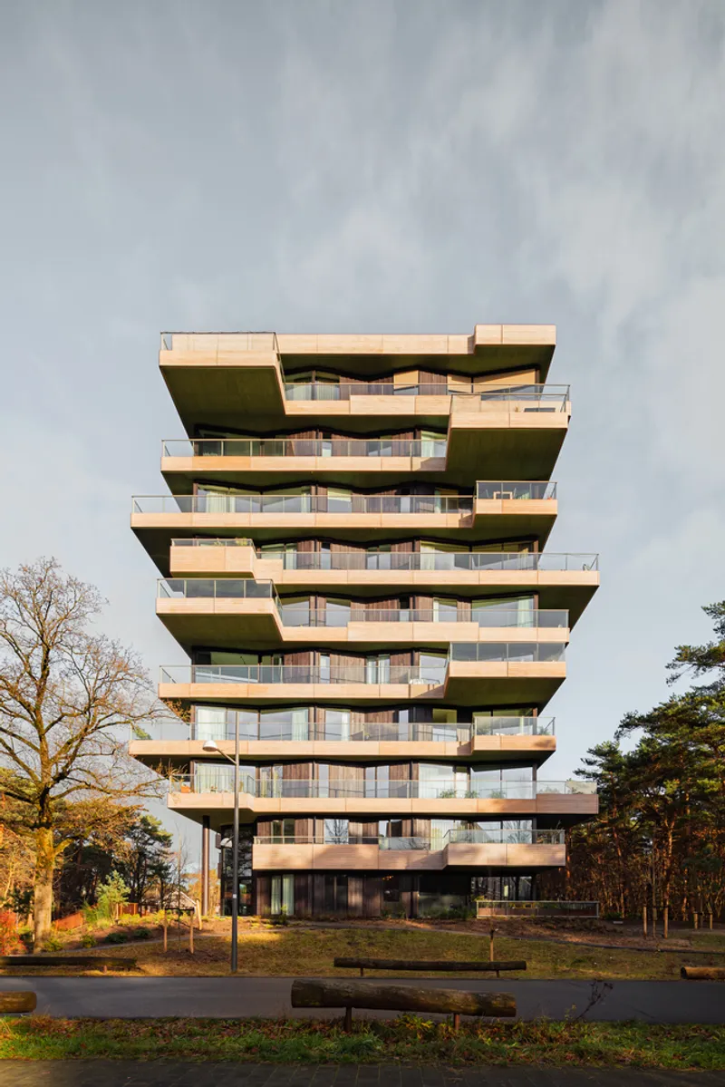Residential tower with offset balconies facing a roadway lined with trees at golden hour