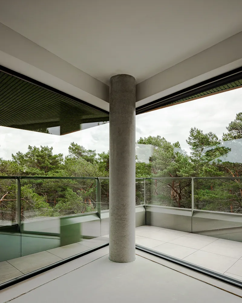 Corner terrace with concrete column, green soffit panels, and glass railings overlooking pine forest