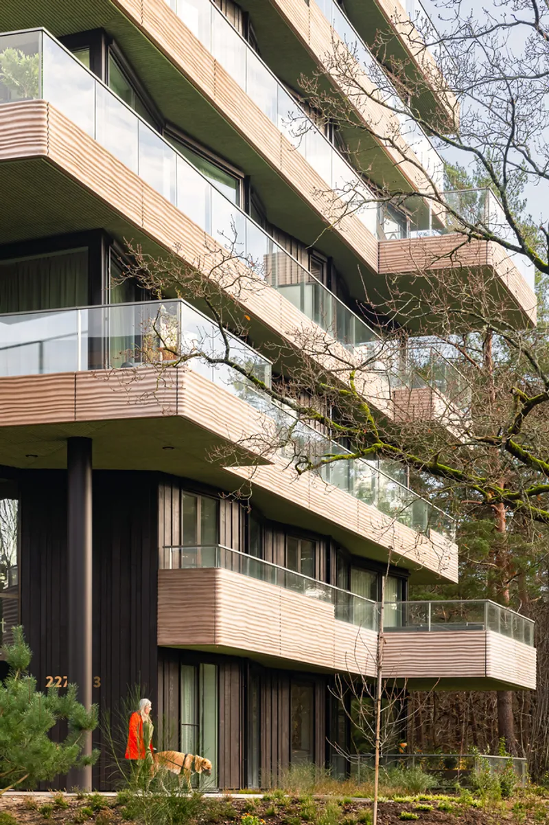 Facade detail of horizontal timber cladding with recessed balconies and a person walking a dog