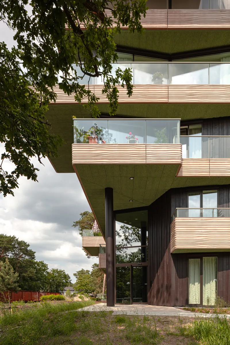 Ground-level entrance with dark timber column and corrugated green soffit beneath cantilevered upper floors