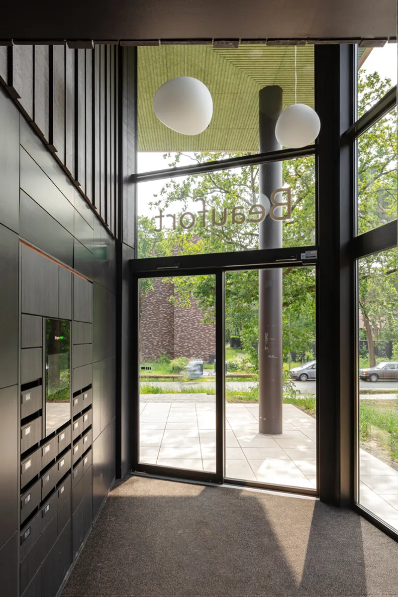 Double-height lobby with black-framed glass doors, mailbox wall, and two globe pendant lights