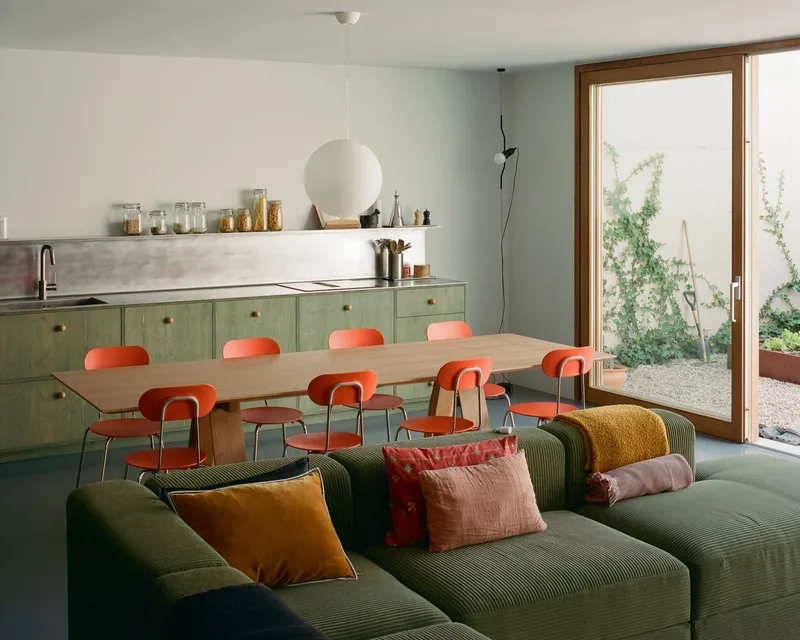 Open-plan kitchen and dining space with green cabinetry and timber table beneath a sphere pendant
