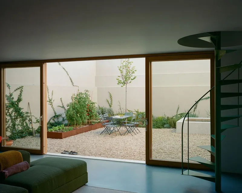Floor-to-ceiling timber-framed sliding doors opening onto a gravel courtyard with planted beds and young tree