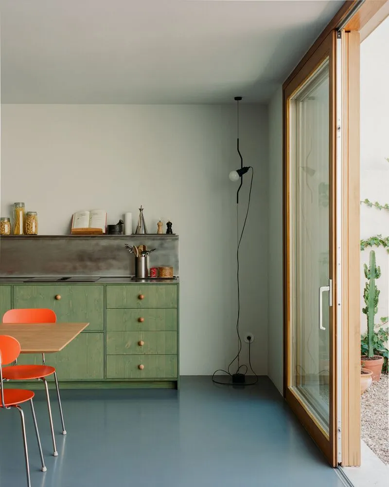 Kitchen corner with green-painted plywood cabinetry and wall-mounted pendant beside timber sliding doors