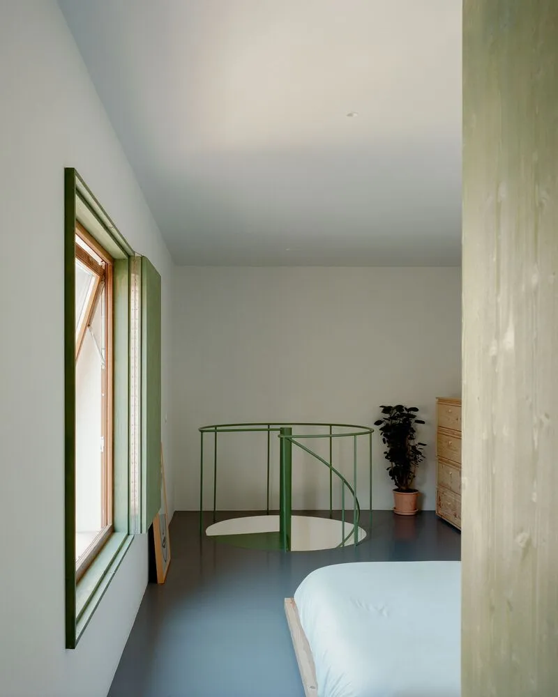 Upper-level bedroom with green window reveal and steel balustrade enclosing the spiral stair opening