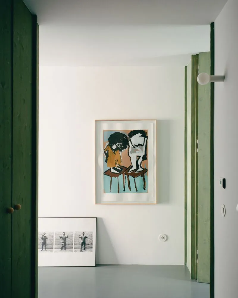 Interior corner with green timber door frames and framed artworks leaning against white walls