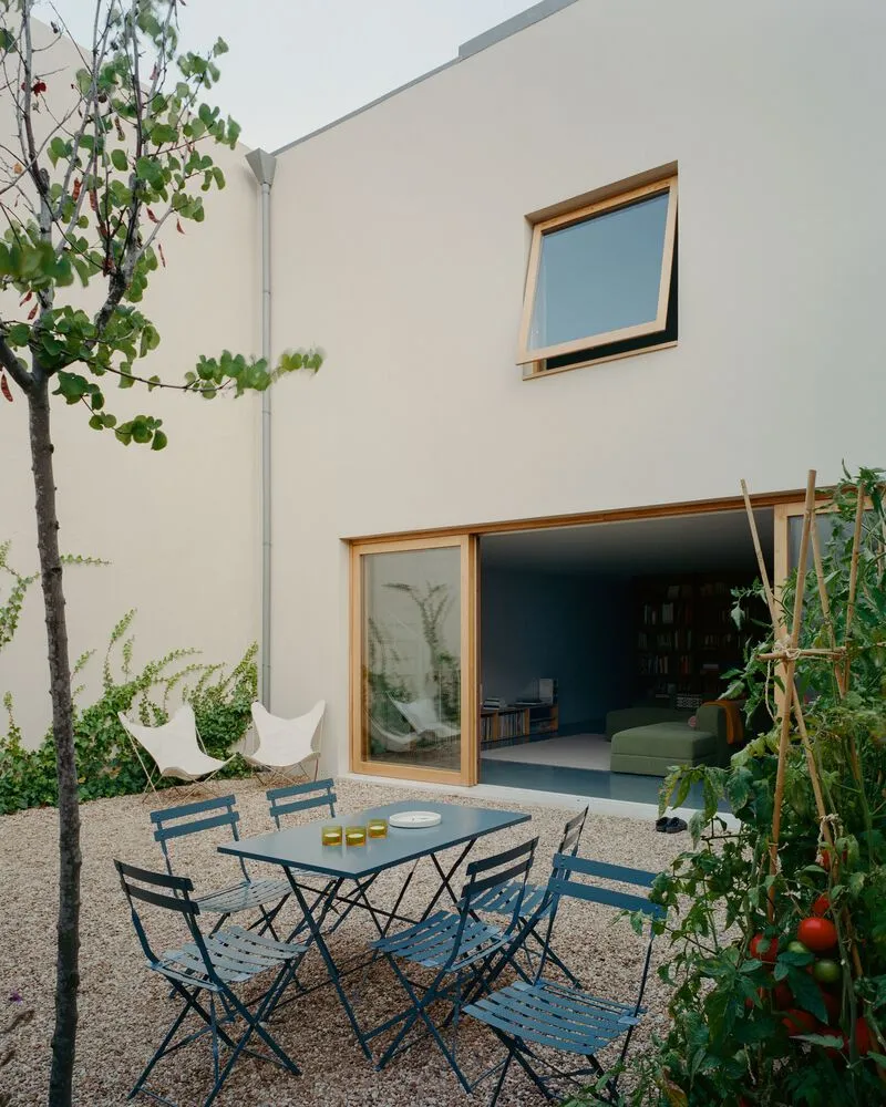 White rendered courtyard facade with timber-framed sliding doors and awning window overlooking a gravel terrace