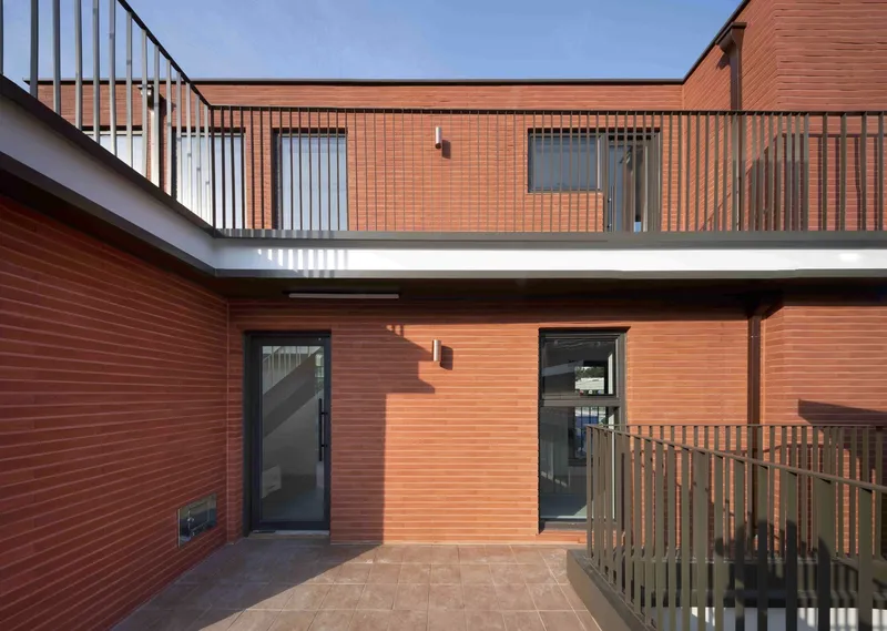Courtyard with red tile facades, black entry doors, and metal railings under afternoon sun