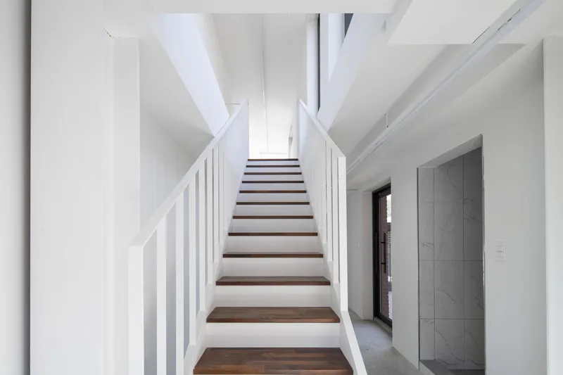 Interior staircase with white vertical railings and dark timber treads beneath angular skylight