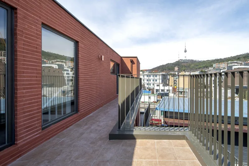 Rooftop terrace with red brick cladding and vertical wood slat railing overlooking hillside neighborhood
