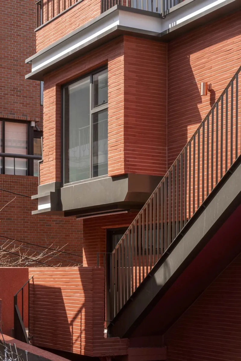 Corner detail of projecting window bay with horizontal brick panels and metal stair railing in bright light