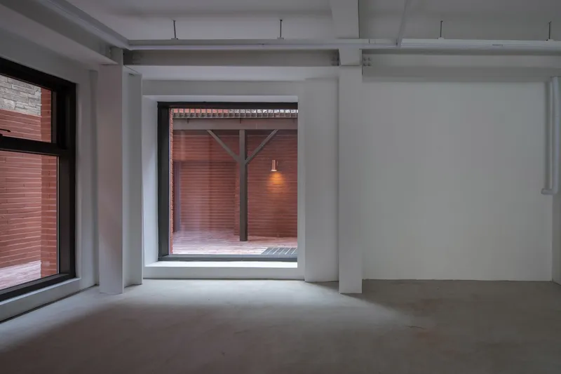 Interior room with polished concrete floor looking through framed opening to red brick courtyard