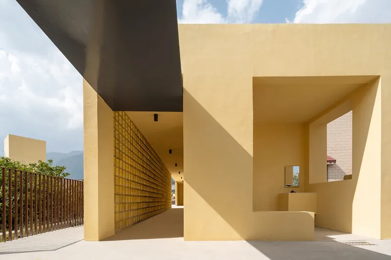 Covered walkway with perforated brick screen and yellow stucco walls under midday sun
